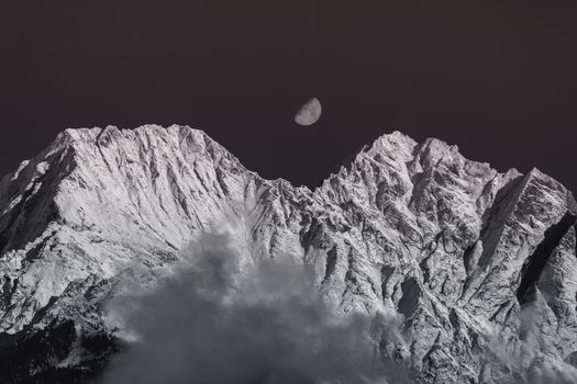 月光下，白雪皑皑的山峰呈现出单色景色，云层环绕