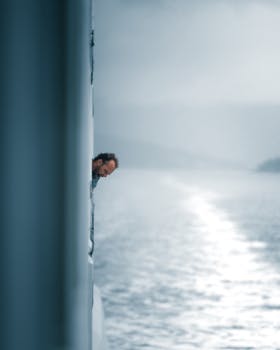 A man leans out from a ship, looking at the sea, creating a sense of adventure.