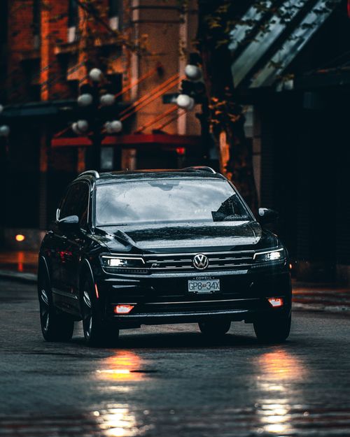 Free A Volkswagen car with headlights on, driving through an urban street at night with wet reflections. Stock Photo