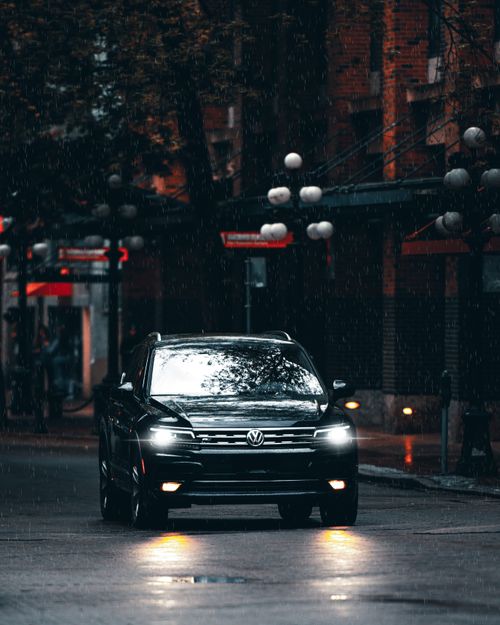 Free A sleek Volkswagen SUV drives through a rainy city street at night, showcasing modern urban transportation. Stock Photo