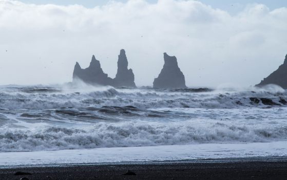 Stormy waves crash at Reynisfjara Beach with striking basalt sea stacks under a cloudy sky.