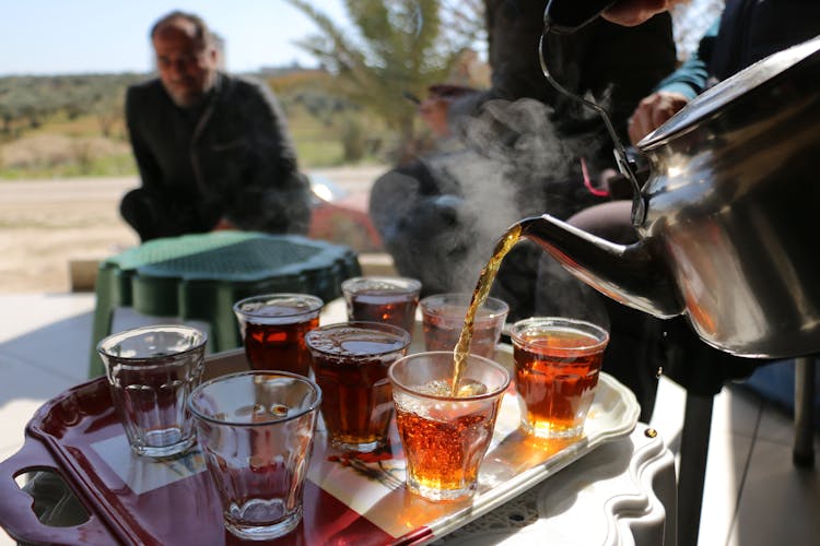 Man Pouring Tea From Kettle Into Glass Cups