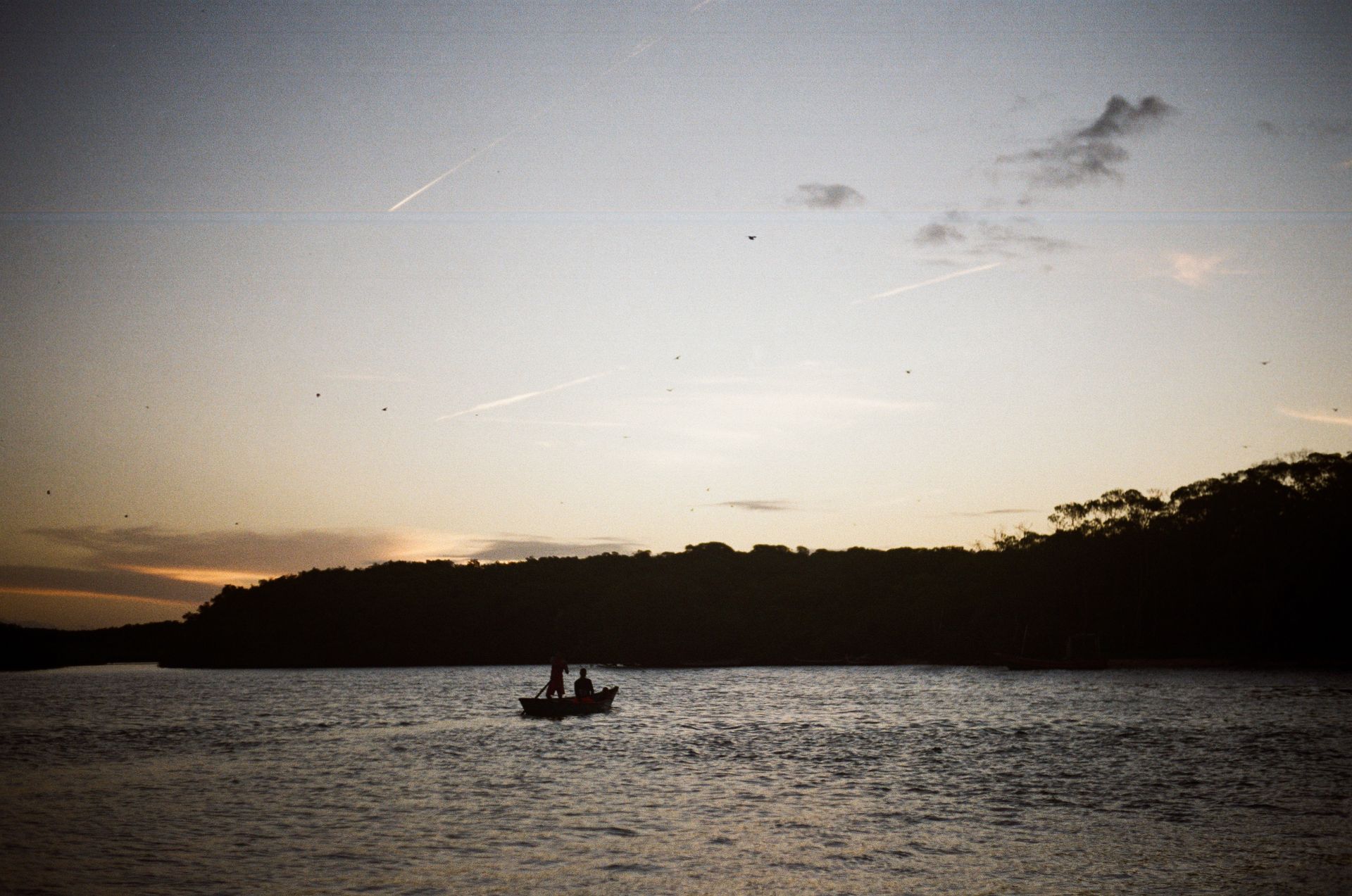 Silhouetted figures rowing at sunset on a tranquil Brazilian lake, capturing a serene moment.