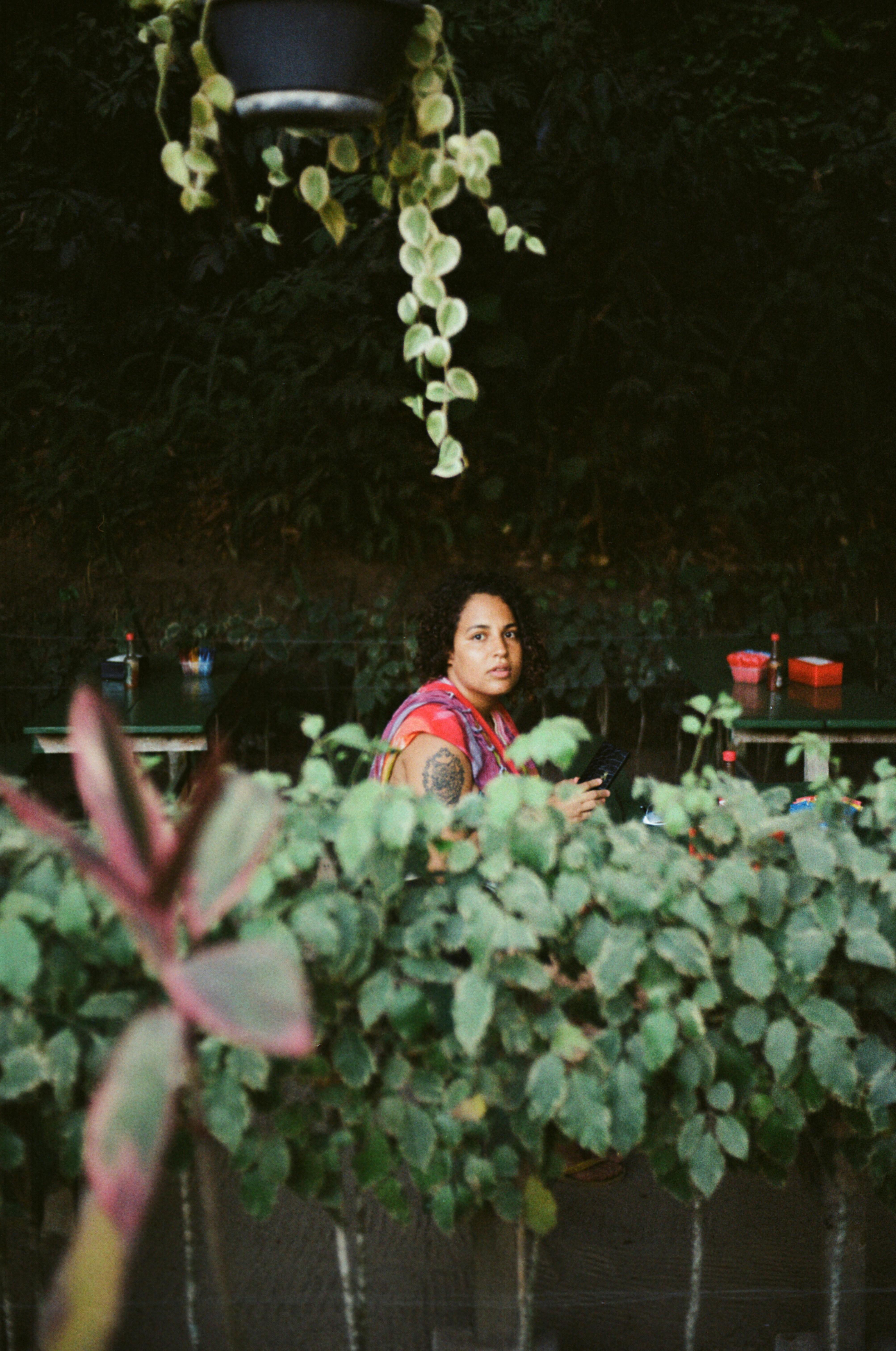 A woman sitting at an outdoor cafe surrounded by lush plants, enjoying nature.
