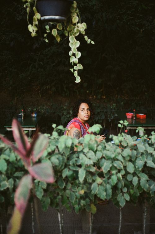 Free A woman sitting at an outdoor cafe surrounded by lush plants, enjoying nature. Stock Photo