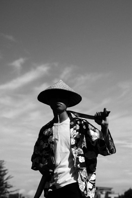 Black and white silhouette of person wearing traditional Asian conical hat with sword.