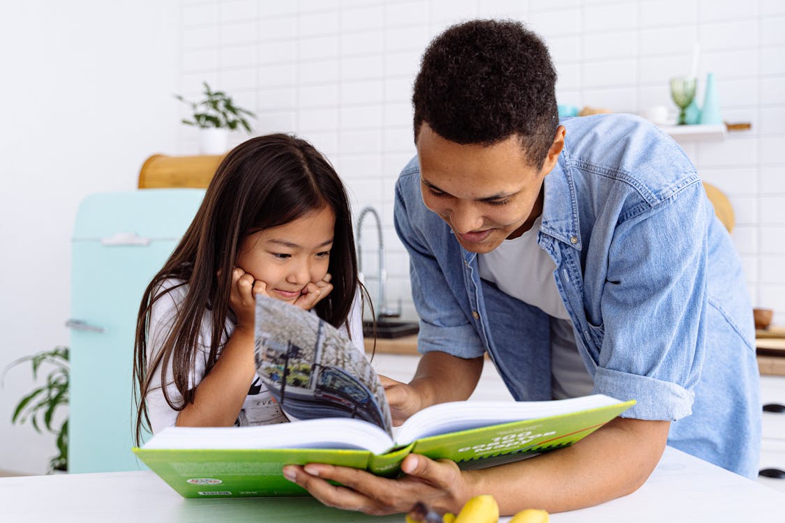 Free Photograph of a Child Reading a Book with Her Father Stock Photo