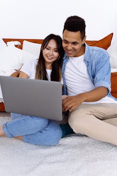Happy interracial couple using laptop together on sofa at home, enjoying leisure time.