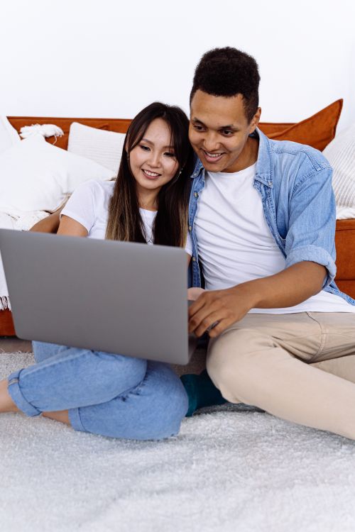 Free Happy interracial couple using laptop together on sofa at home, enjoying leisure time. Stock Photo