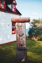 Post with bright title near contemporary cottage facade on grass meadow near sea under blue cloudy sky