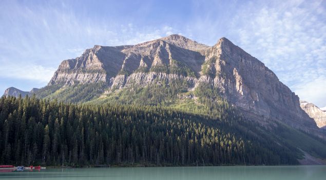 Picturesque view of Lake Louise with towering pine forests and rocky mountains under a clear sky.
