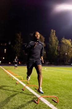 A man trains with agility hurdles on an outdoor track at night, focused and determined.