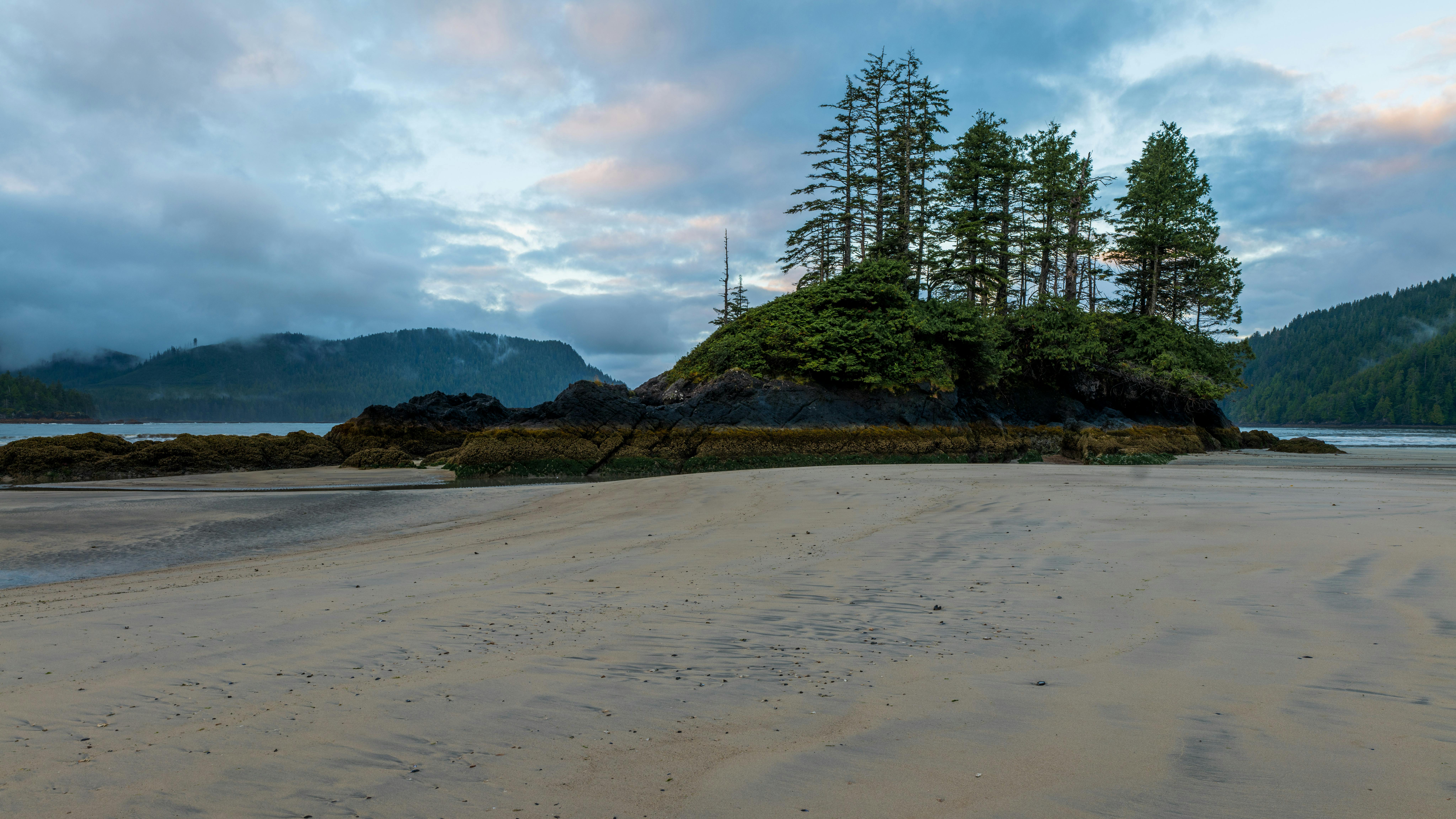 Prescription Goggle Inserts - A tranquil scene of San Josef Bay's sandy beach with lush trees and distant mountains.