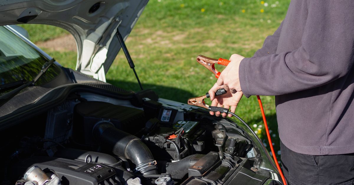 Man using jumper cables on car engine outdoors on a sunny day. Vehicle maintenance and repair concept.