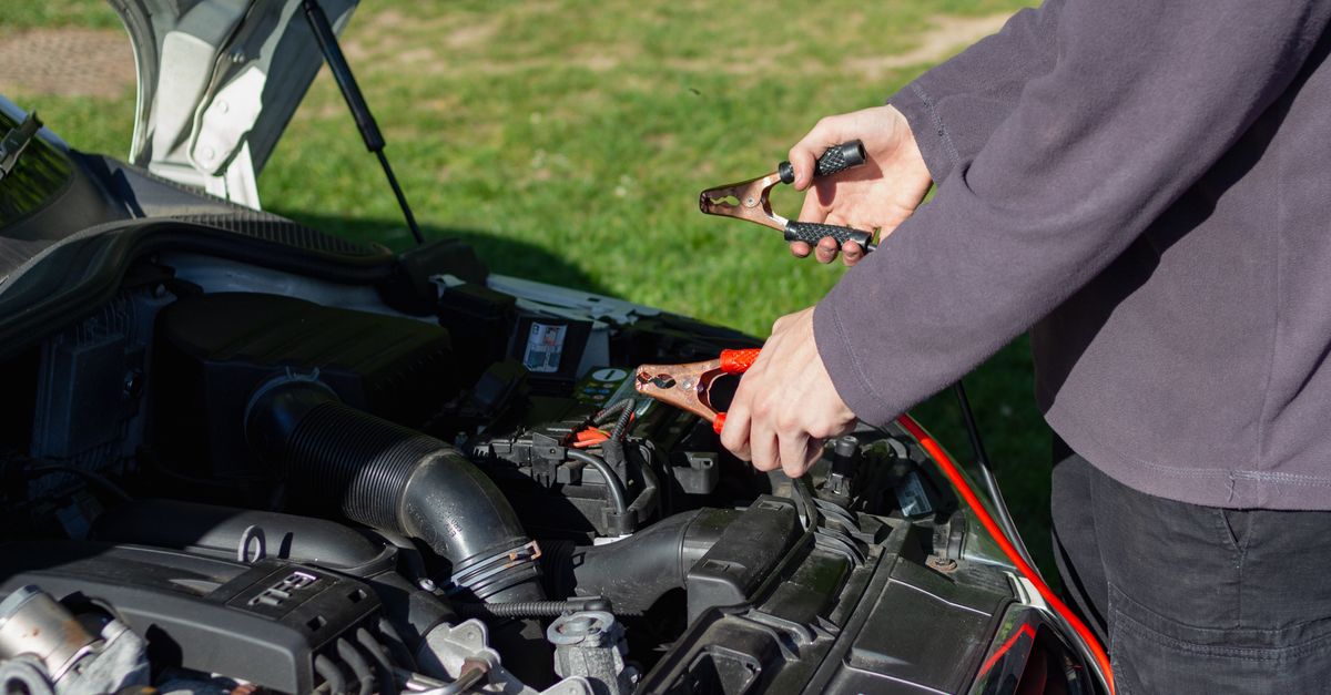 Close-up of mechanic using jumper cables to jump-start a car battery outdoors.