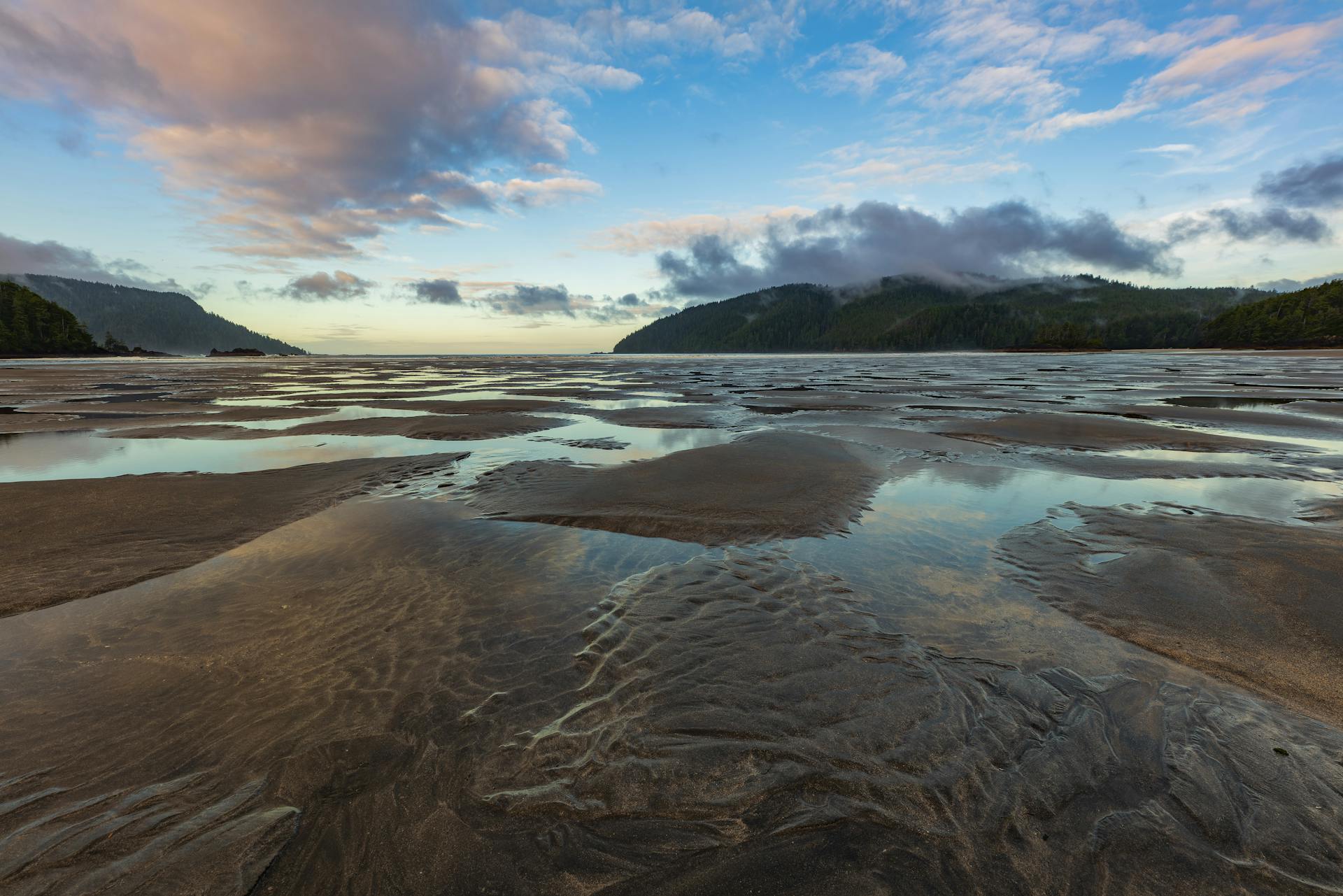 A tranquil view of the shoreline at San Josef Bay with cloud reflections and mountain backdrop.