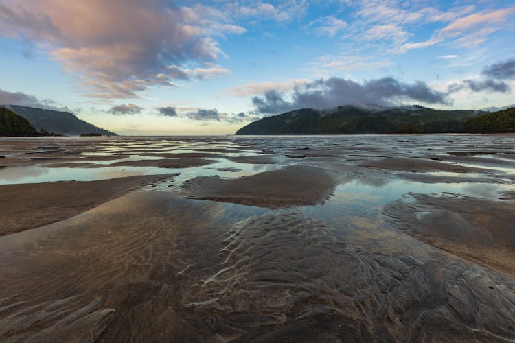 Body Of Water Near Mountain Under Blue Sky