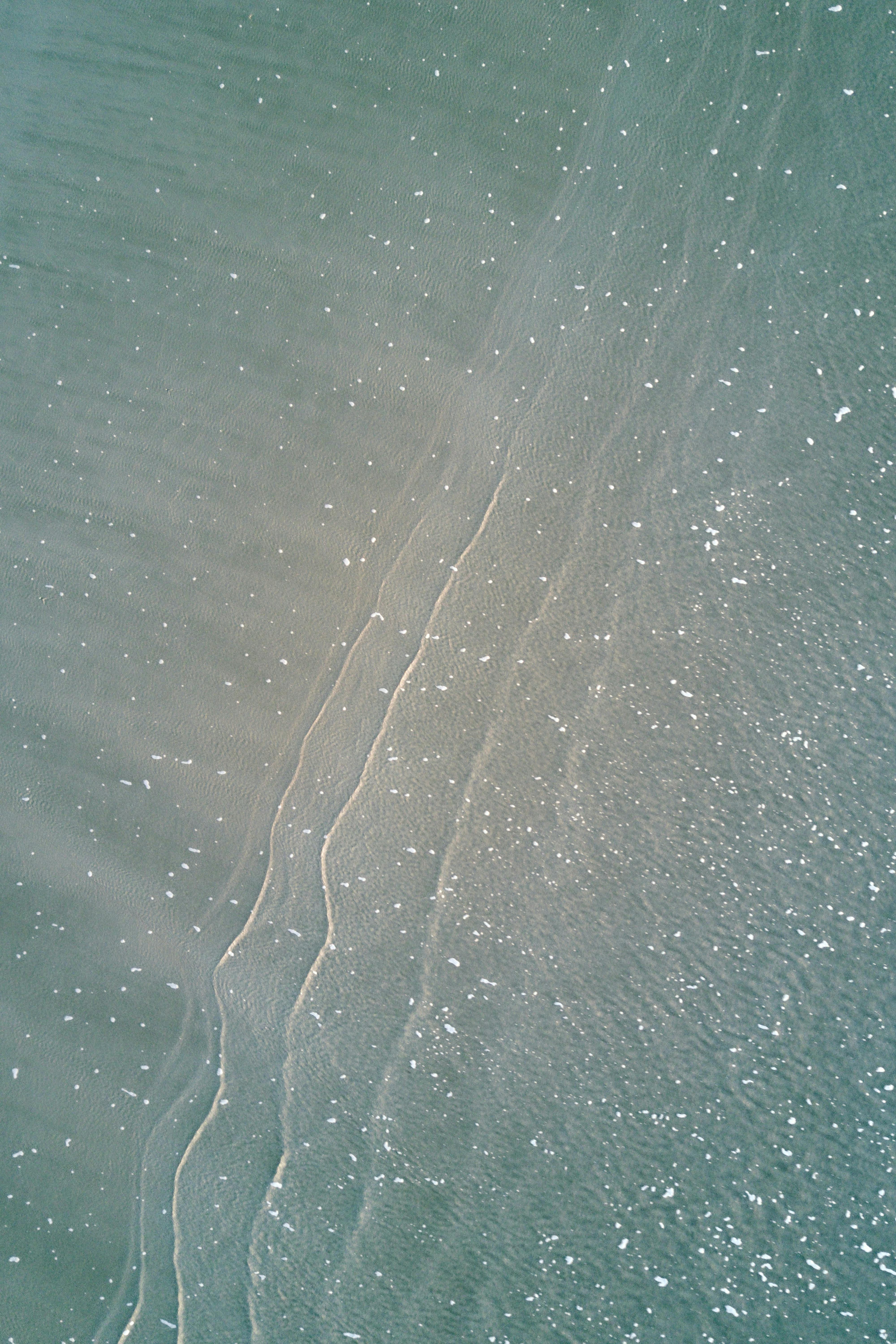 Aerial shot of clear ocean waves gently hitting the sandy shore, reflecting serenity.