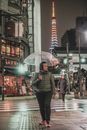 一名亚洲男子撑着伞，走在东京雨夜的街道上，捕捉着这座城市充满活力的夜晚氛围