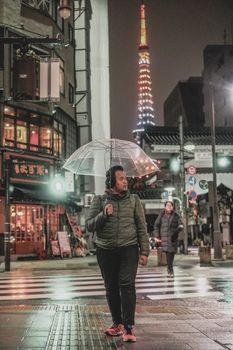 一名亚洲男子撑着伞，走在东京雨夜的街道上，捕捉着这座城市充满活力的夜晚氛围