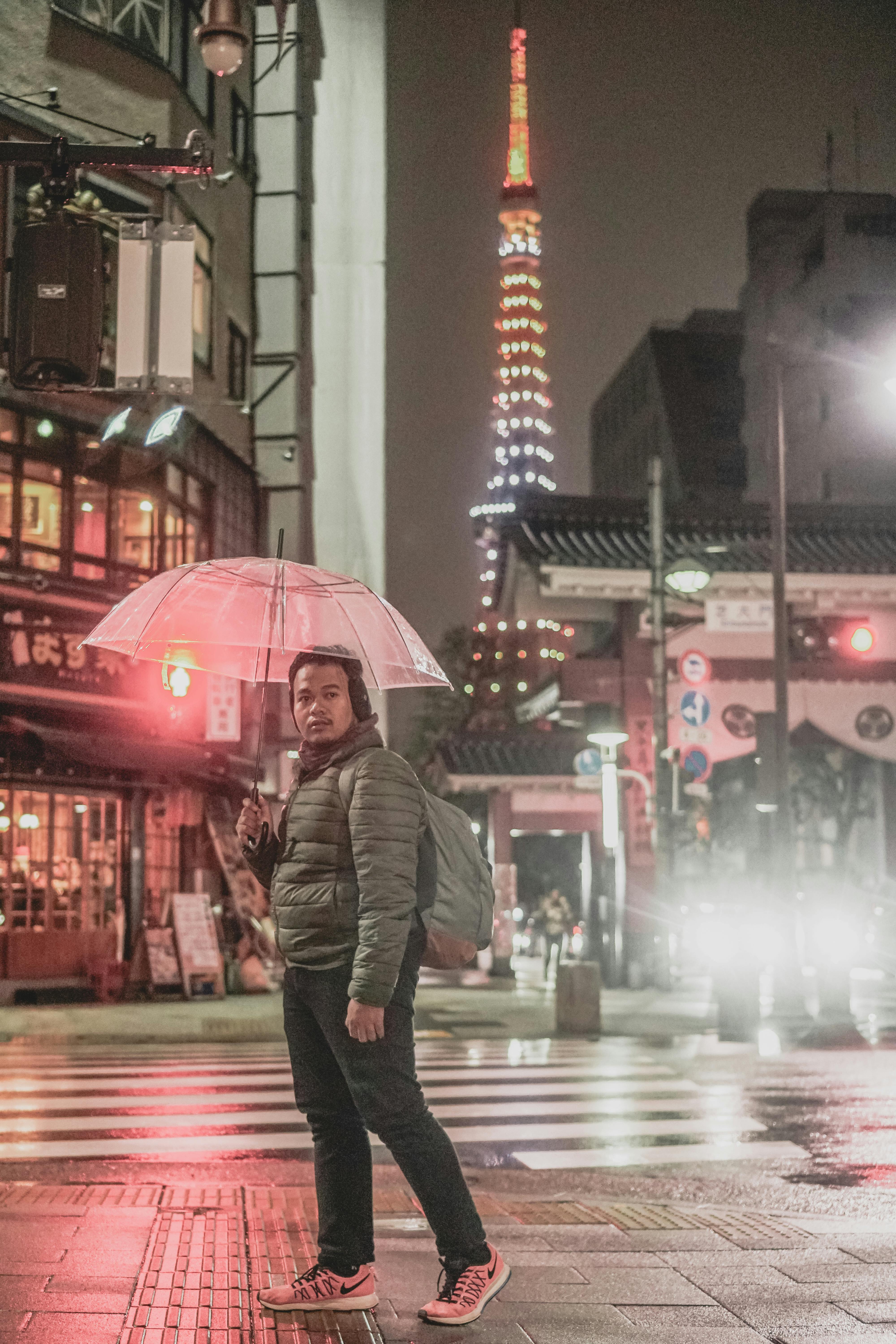 东京塔夜间灯火通明，一名男子在街道上撑着伞