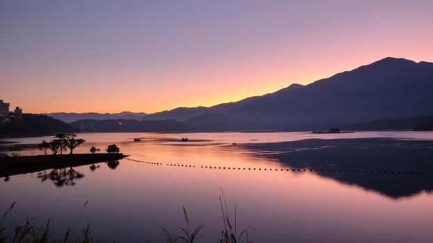 A tranquil lake view at sunset with mountains reflecting in the calm water.