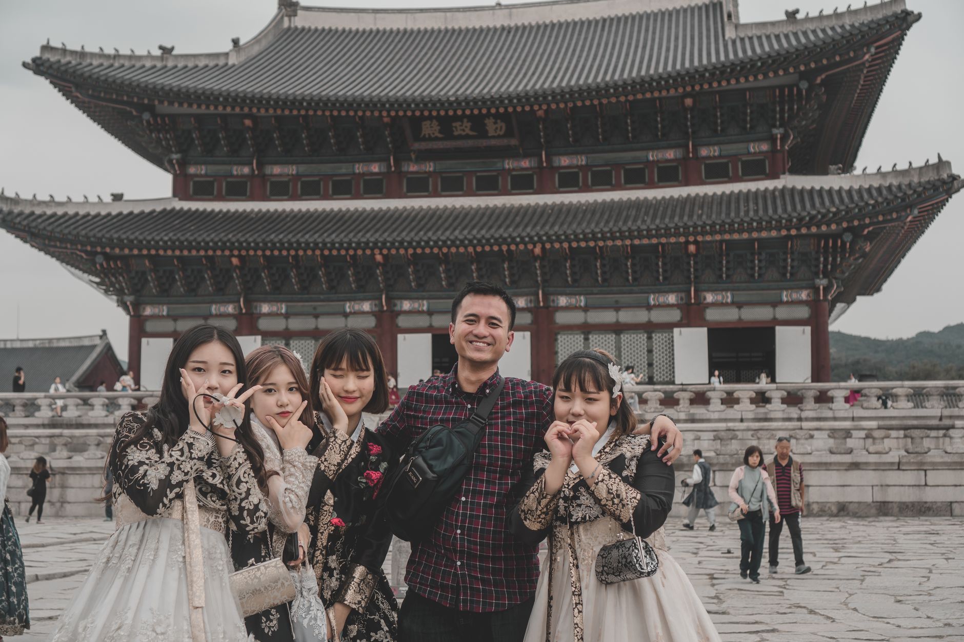 A cheerful group of international tourists wearing various colorful hanbok poses for a photo at Namsan Hanok Village in Seoul, embracing Korean culture.