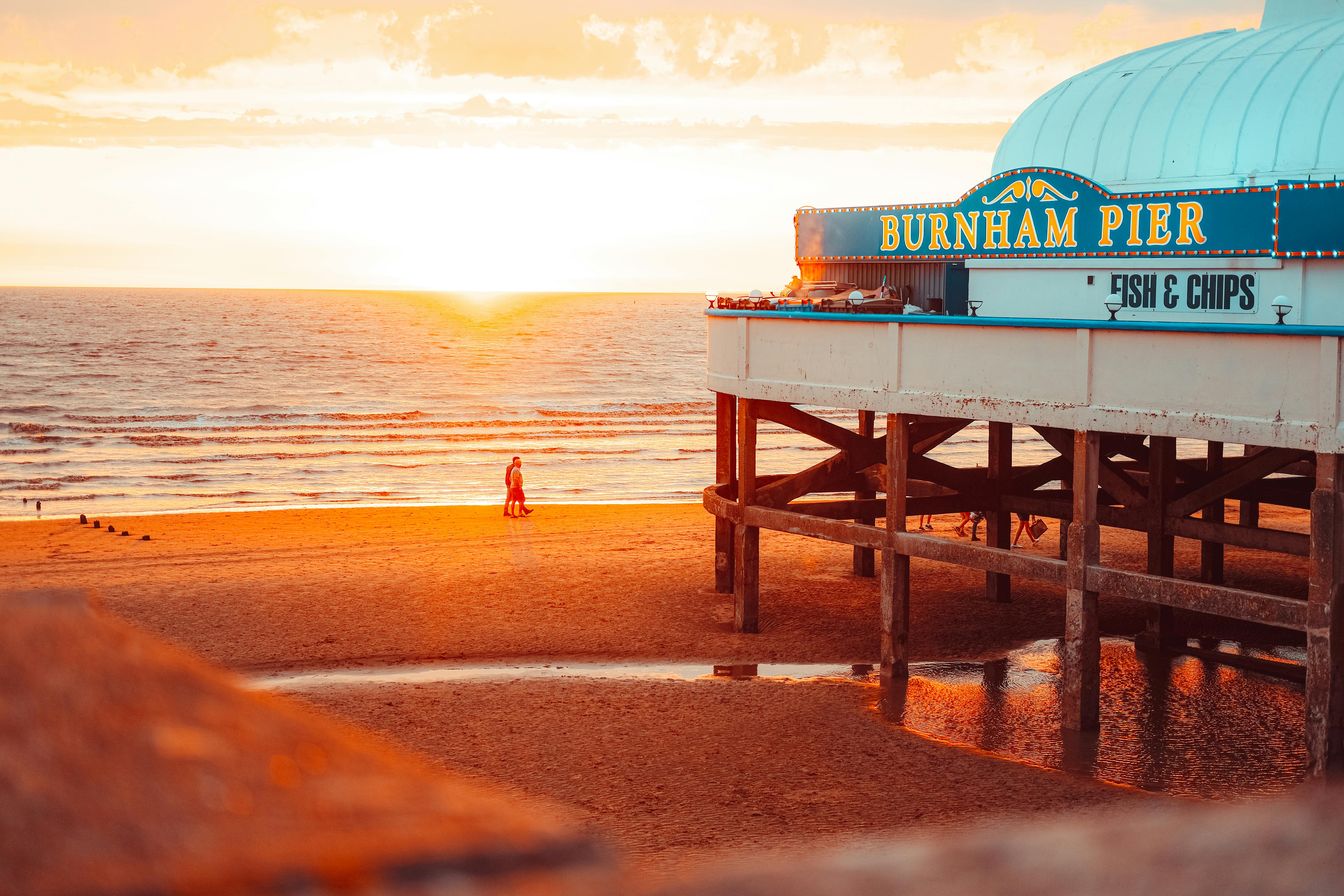 Warm sunset view of Burnham Pier with beachgoers and scenic coastal horizon.