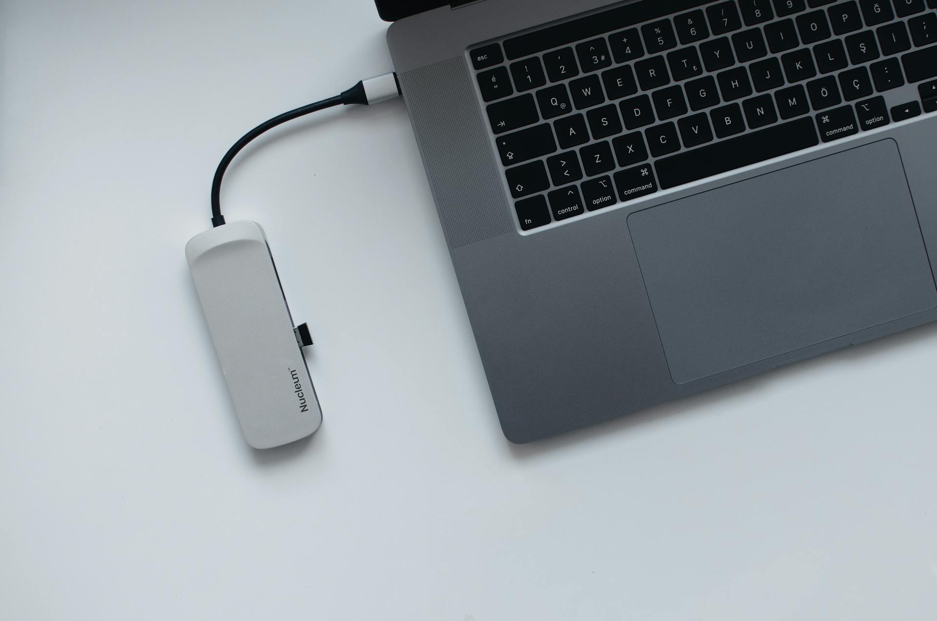 A sleek laptop connected to a USB hub on a minimalist white desk. Perfect for tech setups.