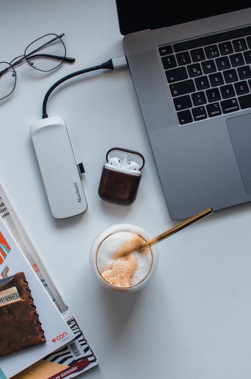 Overhead glass of latte and wallet with eyeglasses and earphones near laptop with USB hub on desk