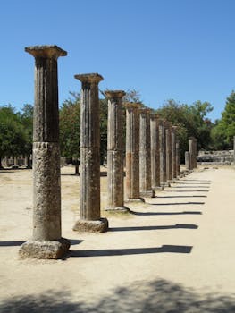 Row of ancient columns under blue sky at historical site Archaia Olympia, Greece.
