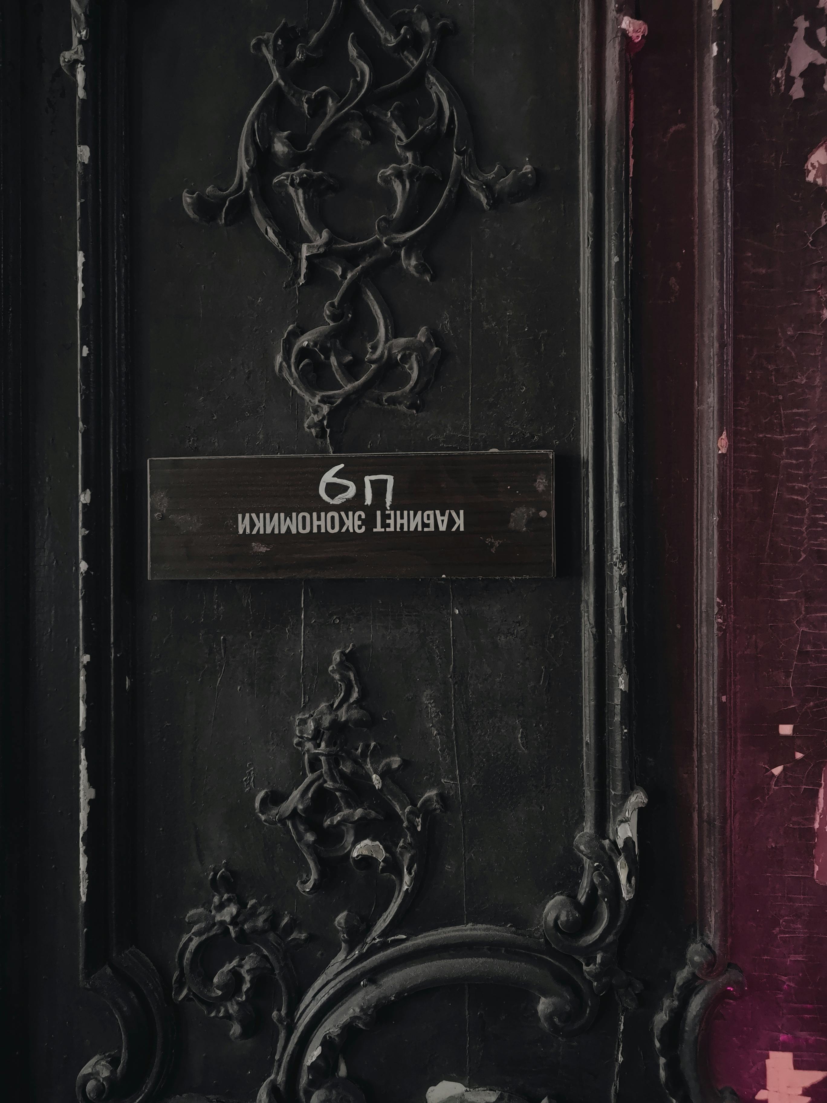 Close-up of a weathered wooden door with ornate carvings and a reversed sign.