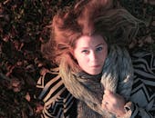 这幅描绘蓝眼金发女子卧于落叶之上的秋季肖像画，显得宁静安详