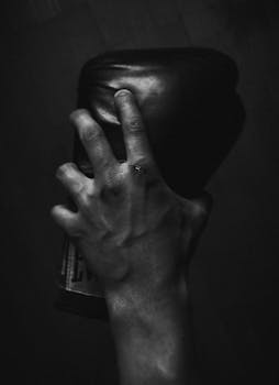 A monochrome image showing a hand gripping a boxing glove, emphasizing texture and strength.