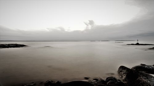 Free A tranquil grayscale seascape with rocks and cloudy horizon captured in long exposure. Stock Photo