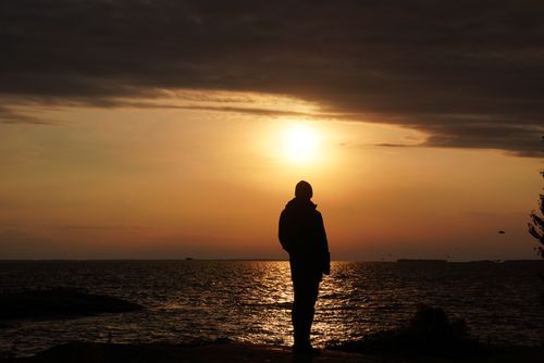 Free A person silhouetted against a vibrant ocean sunset, creating a serene scene. Stock Photo