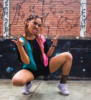Confident woman in streetwear poses by brick and graffiti wall, expressing urban style.