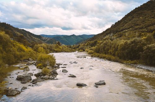 Free A tranquil river meandering through a lush valley with mountains and dense forest surrounding it. Stock Photo