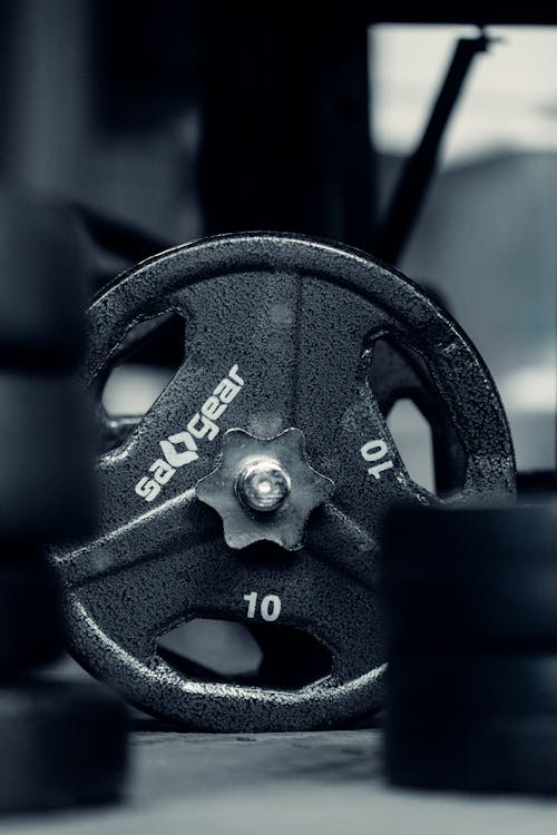 Black and white of big round black disc of dumbbell in sports hall in daytime on blurred background