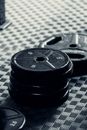 Black and white of big round black weight plates with numbers on surface on plaid rubber mat in daylight