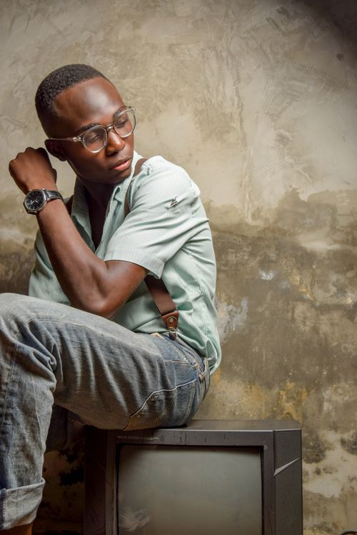 Free Fashionable young man with glasses sitting indoors, posing on an old TV. Stock Photo