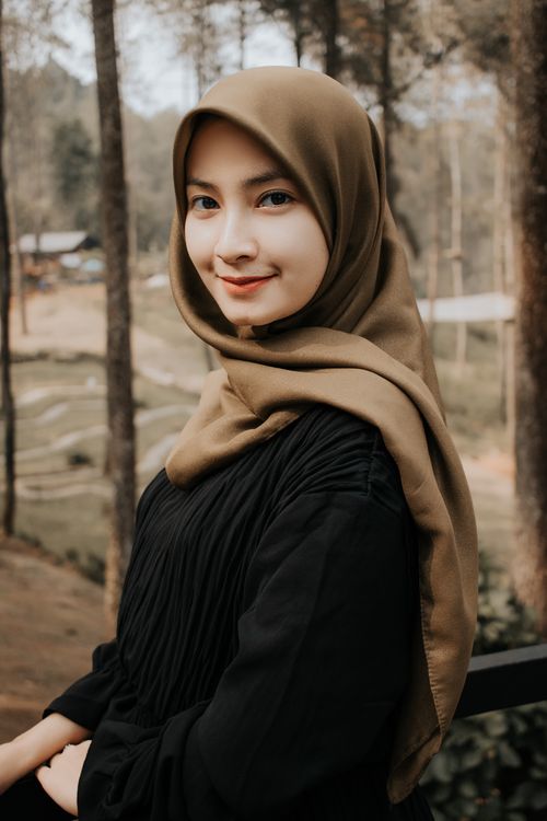 Free Side view attractive young Muslim female wearing traditional hijab standing in lush green park and looking at camera with pretty smile Stock Photo