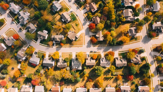 Aerial view of residential building roofs between lawns with colorful trees and roadways in fall