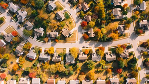 Free Aerial view of residential building roofs between lawns with colorful trees and roadways in fall Stock Photo