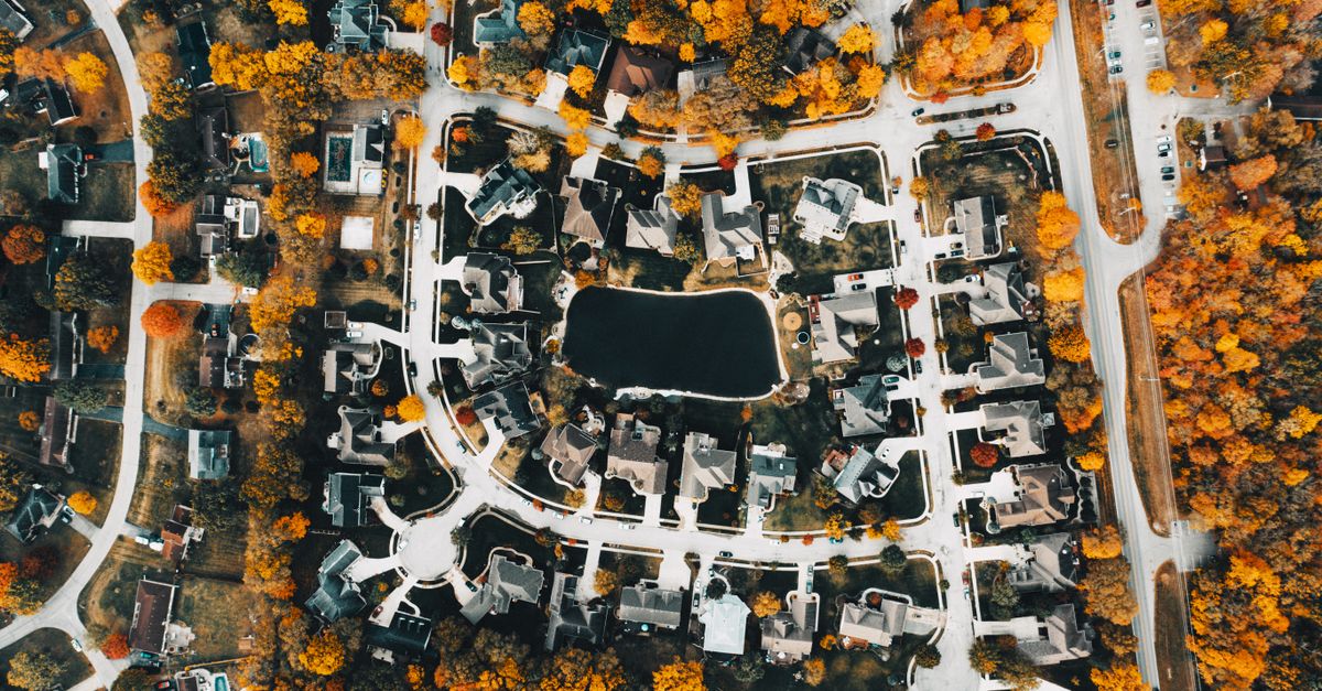 Aerial view of building roofs near artificial pond and roadways with autumn trees in suburb