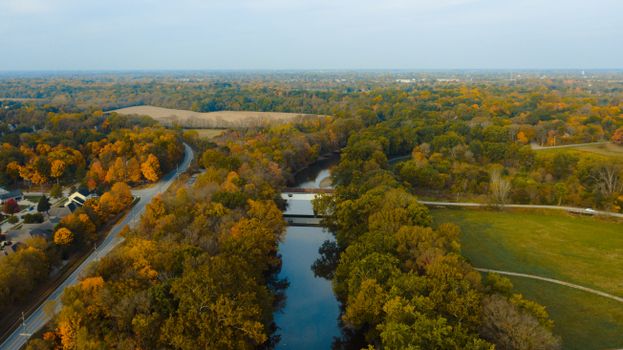 Aerial view of bridge above river between roadway and lush woods near lawn in suburb