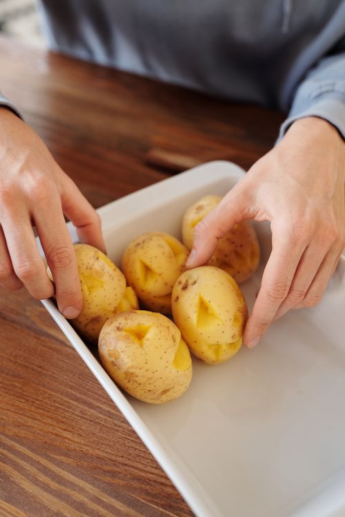 Free Hands arranging raw potatoes in a dish, ideal for cooking tutorials or organic food themes. Stock Photo
