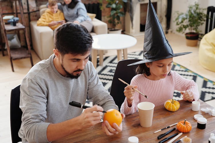 Father And Daughter Decorating Pumpkin And An Orange Fruit