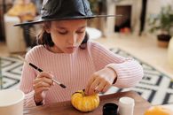 为了体验万圣节的乐趣，一个戴着女巫帽的小女孩在室内画了一个小南瓜