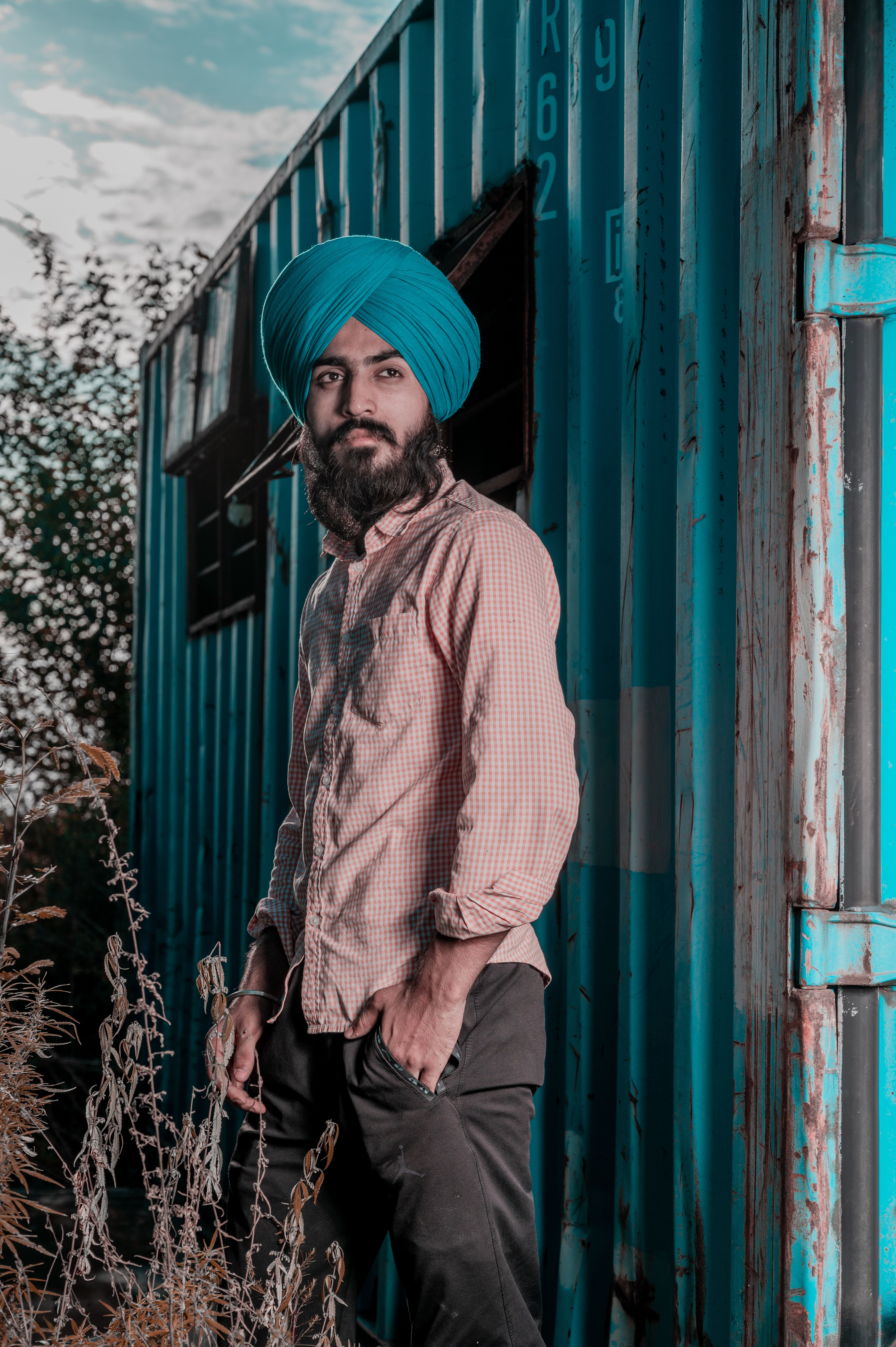 A stylish man with a turban posing next to a blue container outdoors.